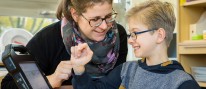 Ergotherapeutin arbeitet mit einem Jungen am Talker.