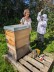 Eine Lehrerin und eine Schülerin stehen vor einem Bienenkorb. Die Schülerin in Schutzkleidung freut sich.